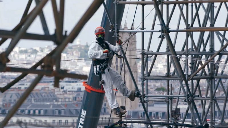 un cordiste essaye d’installer des éléments de soutien pour consolider l’échafaudage démoli par la chute de la flèche.